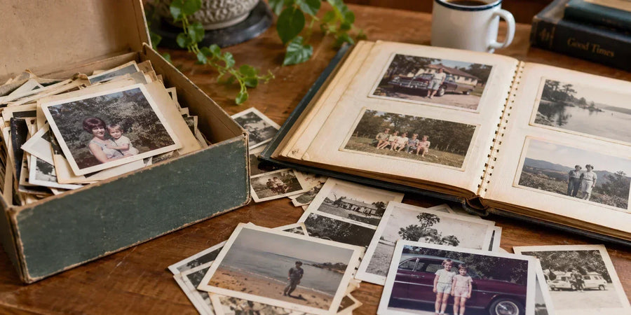 Box of loose family photographs and a 1970s album spread across a wooden table